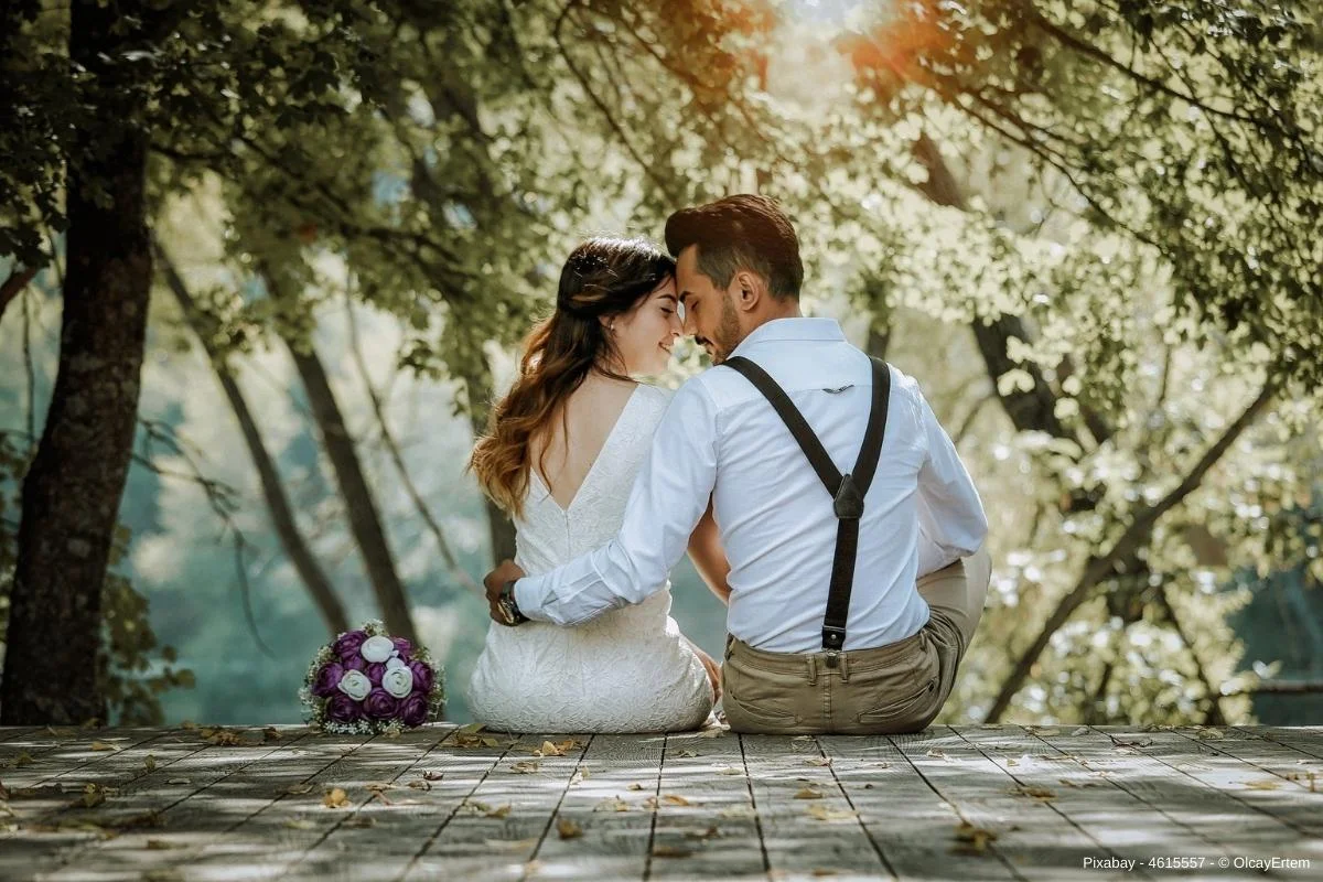 Brautpaar sitzt auf einer Holzterasse mit Bäumen im Hintergrund - In diesem Beitrag erfahren Sie wissenswerte Informationen zum Thema Hochzeit - 11 Tipps für Ihre Traumhochzeit.